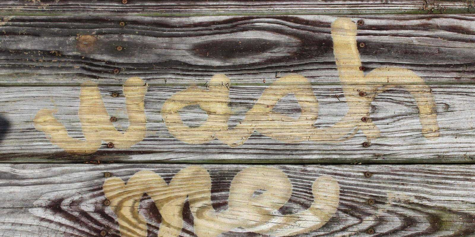 The words “wash me” pressure washed into an old, weathered deck